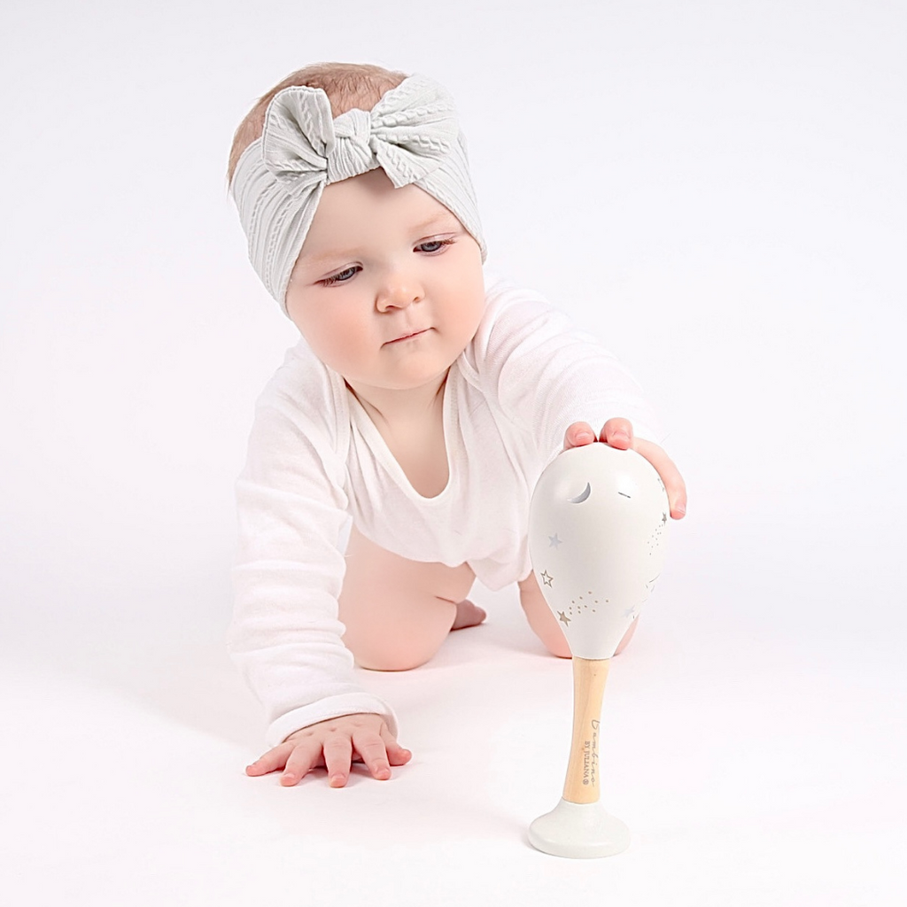 A baby playing with a wooden maraca from their 3-6 month subscription box.