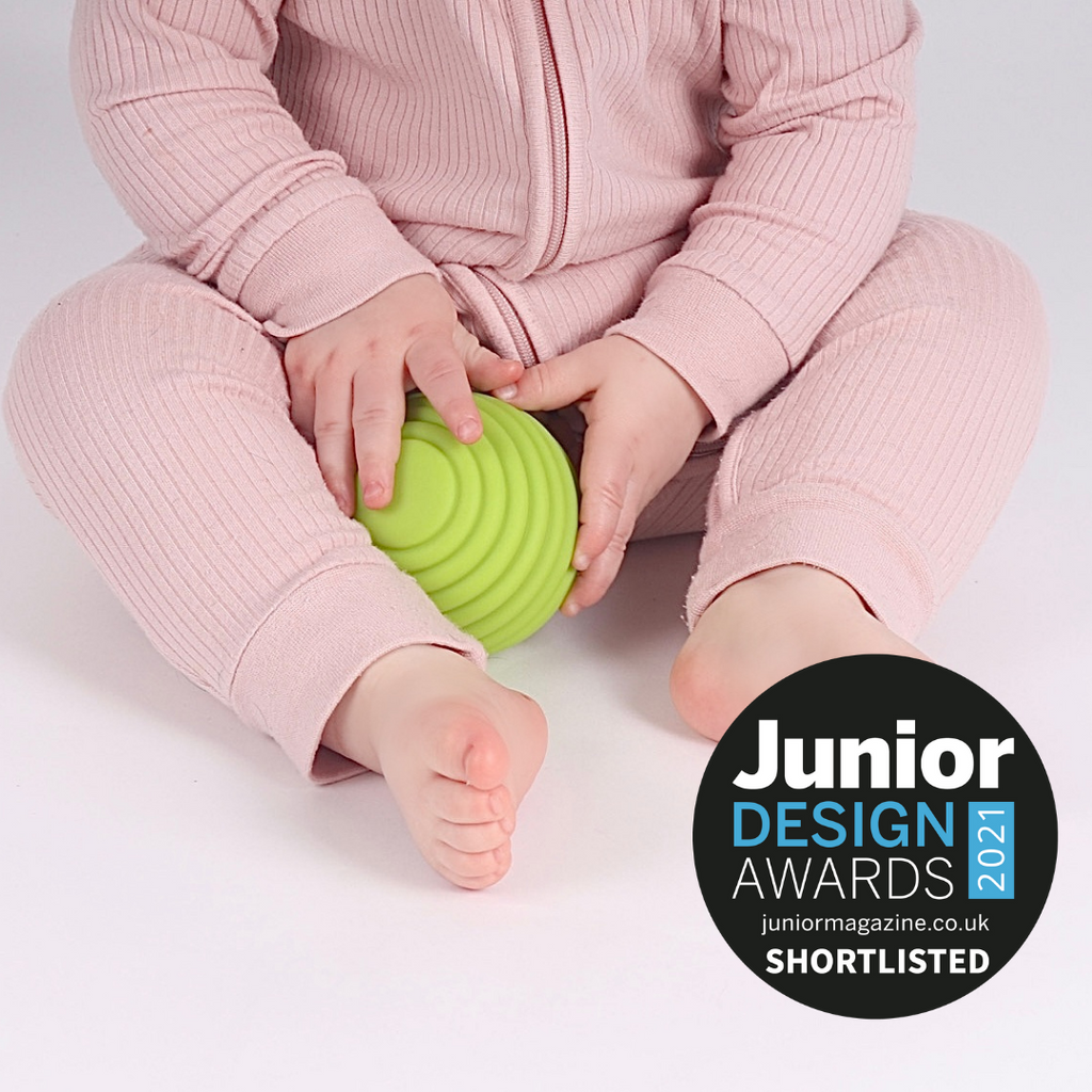 A baby playing with a green textured sensory ball.