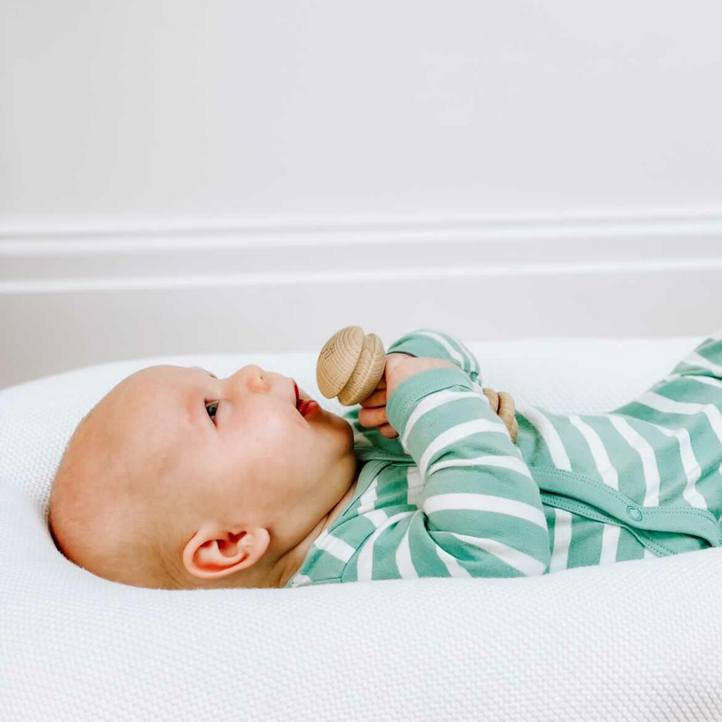 A baby holding a wooden teething beaded rattle from their 3-6 month baby's first year subscription box.