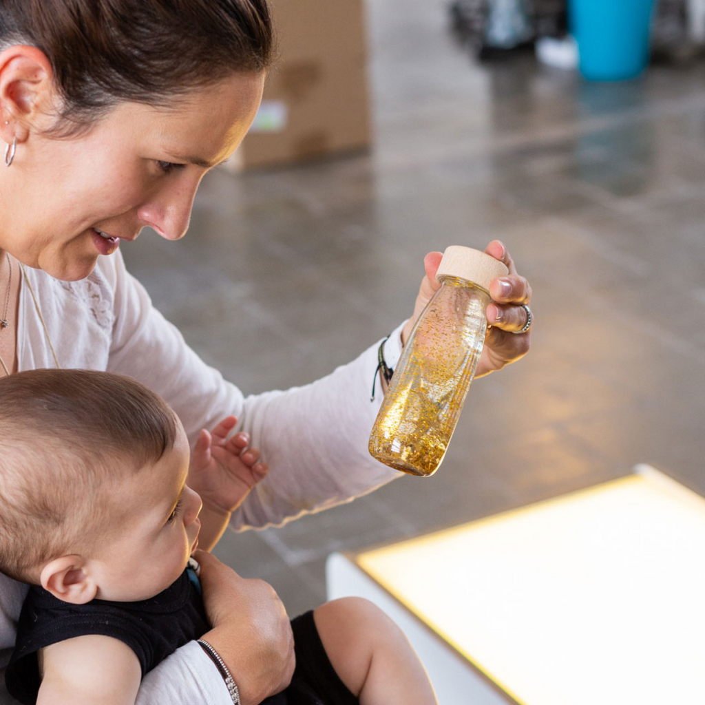 Mum showing a baby a Petit Boum gold sensory float bottle.