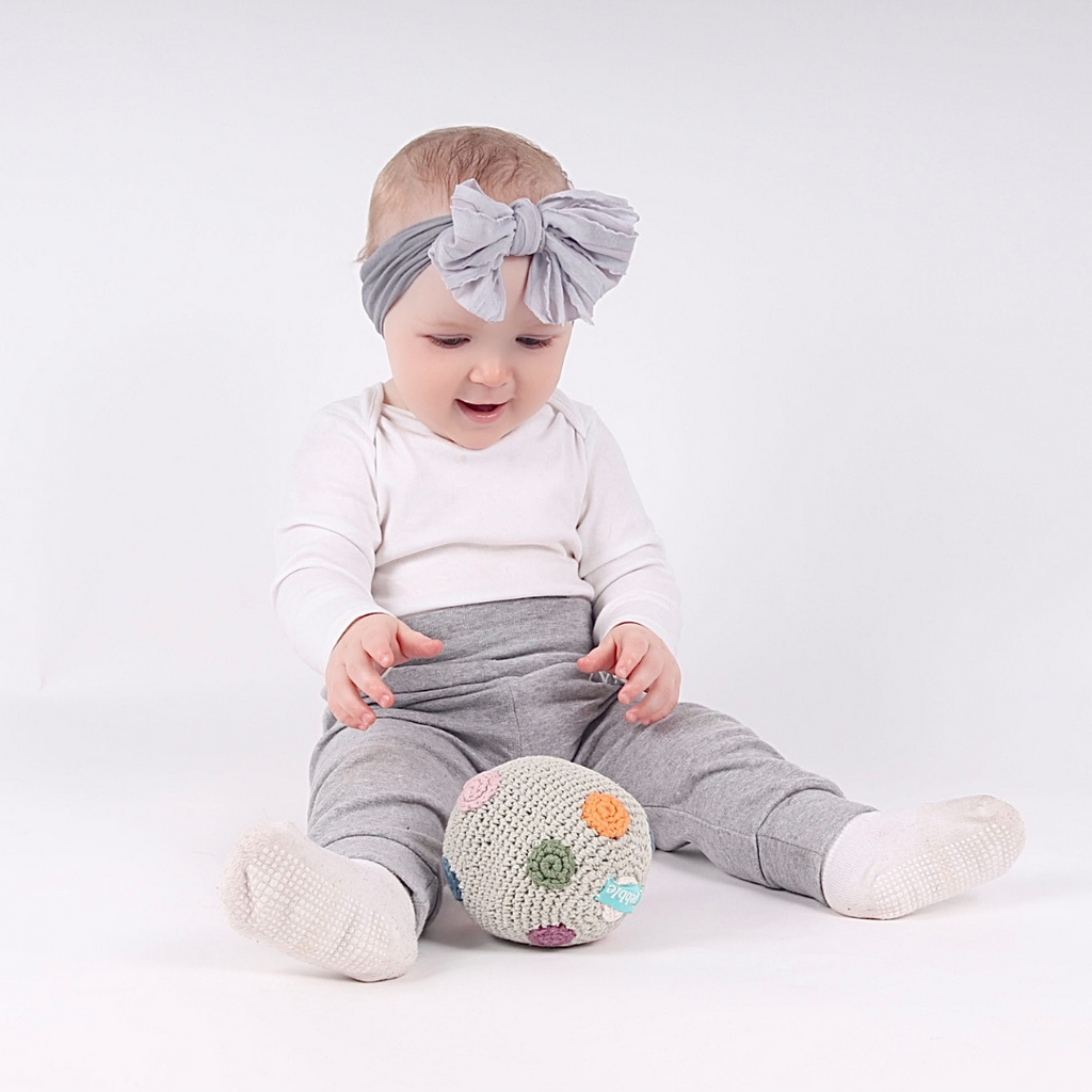 A baby playing with a soft rattle ball from their 3-6 month subscription box.