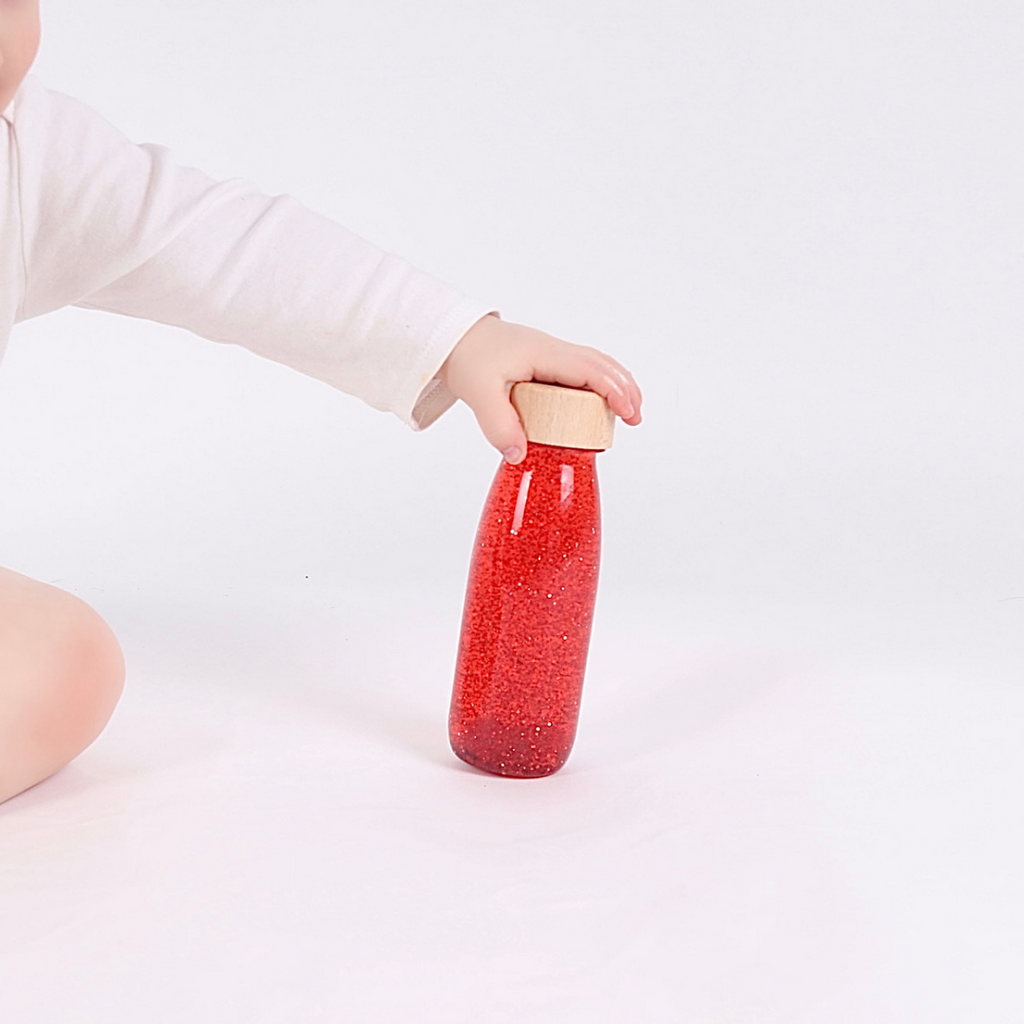 Sensory play with a red Petit Boum Sensory Float Bottle from the 3-6 month subscription box.