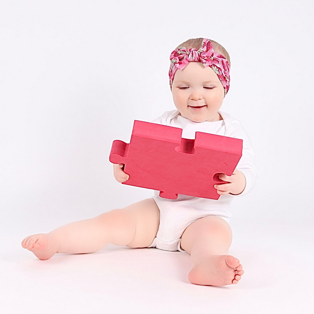 A baby playing with a baby safe TickIt foam jigsaw mirror from their 3-6 month subscription box.