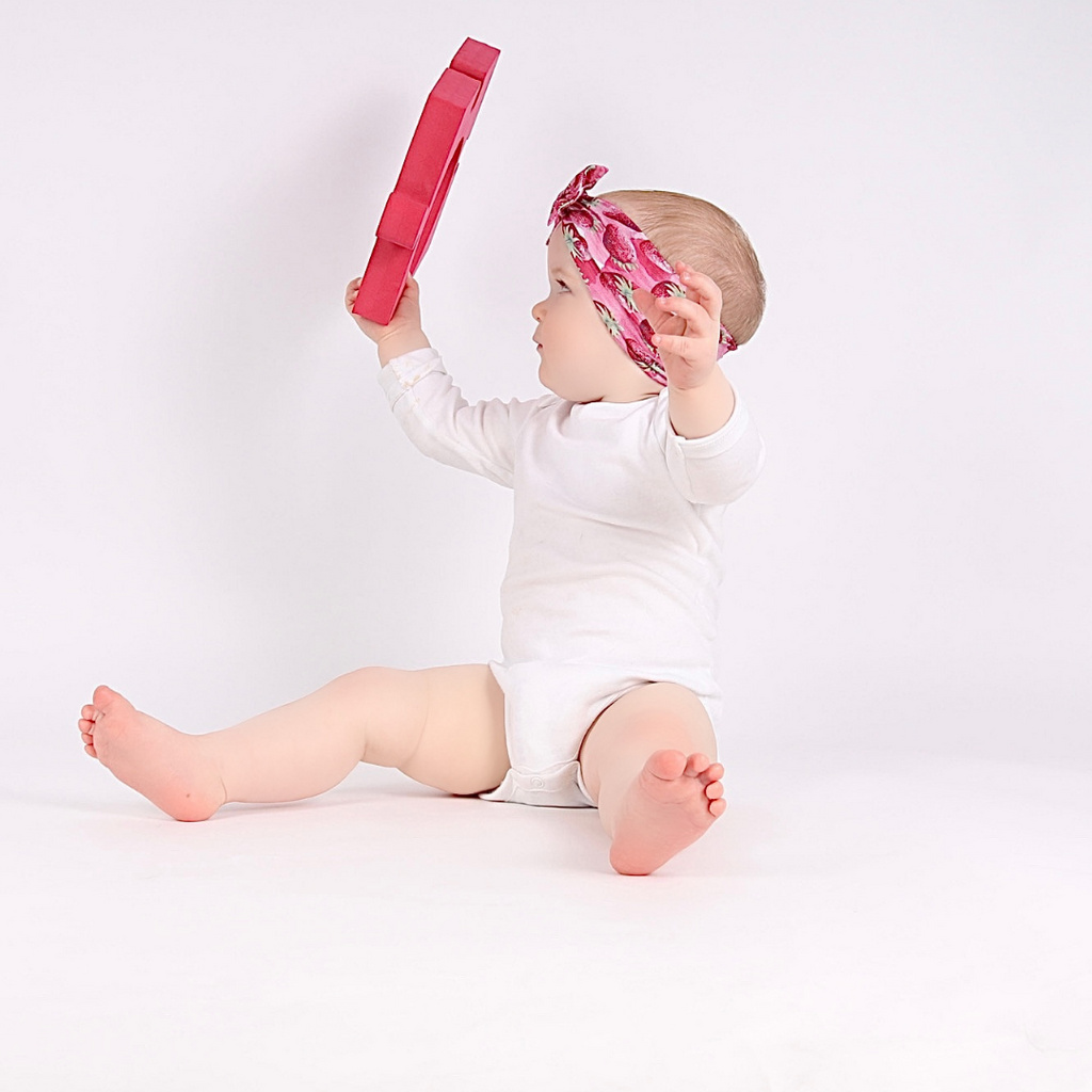 A baby looking at their reflection whilst holding a baby safe foam TickIt Jigsaw Mirror  from the 3-6 month subscription box.