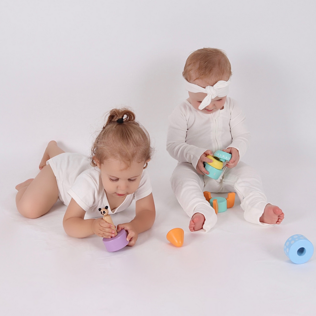 Two baby's playing with the Studio Circus Peekaboo Panda Stacking Wooden Rocket Tower. One laying on their tummy with the panda and one sitting stacking pieces.