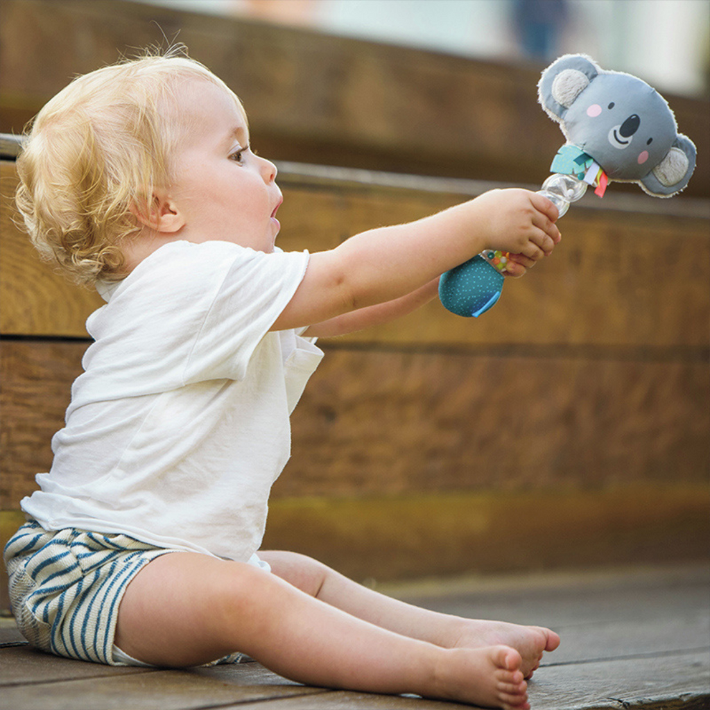 A baby lifting the taf toys koala rainstick baby rattle