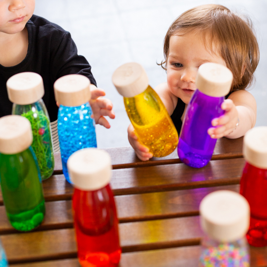 A baby reaching out for various Petit Boum sensory float bottles.